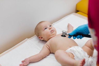 Çocuk doktoru, bebeğini muayene ediyor. Çocuğun kalp atışlarını dinlemek için steteskop kullanan bir doktor. Kapat..