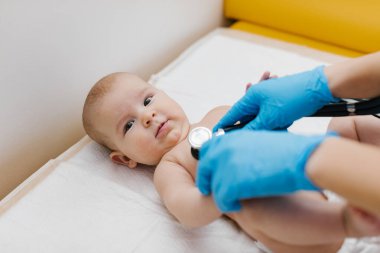 Çocuk doktoru, bebeğini muayene ediyor. Çocuğun kalp atışlarını dinlemek için steteskop kullanan bir doktor. Kapat..