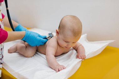 Pediyatrist hastanede yeni doğmuş bir bebeği muayene ediyor. Çocuk doktoru bebeğin kalp atışlarını dinlemek için steteskop kullanıyor..