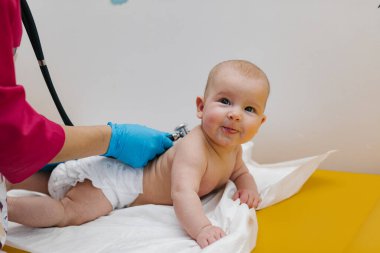 Pediyatrist hastanede yeni doğmuş bir bebeği muayene ediyor. Çocuk doktoru bebeğin kalp atışlarını dinlemek için steteskop kullanıyor..