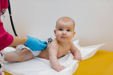 Pediyatrist hastanede yeni doğmuş bir bebeği muayene ediyor. Çocuk doktoru bebeğin kalp atışlarını dinlemek için steteskop kullanıyor..