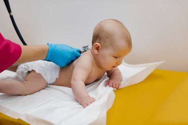 Pediyatrist hastanede yeni doğmuş bir bebeği muayene ediyor. Çocuk doktoru bebeğin kalp atışlarını dinlemek için steteskop kullanıyor..