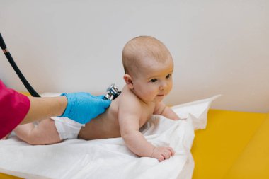 Pediyatrist hastanede yeni doğmuş bir bebeği muayene ediyor. Çocuk doktoru bebeğin kalp atışlarını dinlemek için steteskop kullanıyor..