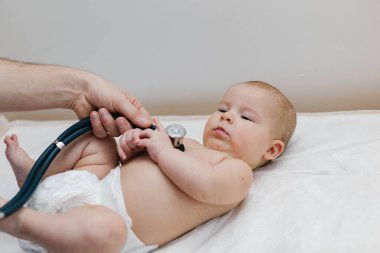 Çocuk doktoru, bebeğini muayene ediyor. Çocuğun kalp atışlarını dinlemek için steteskop kullanan bir doktor. Kapat..