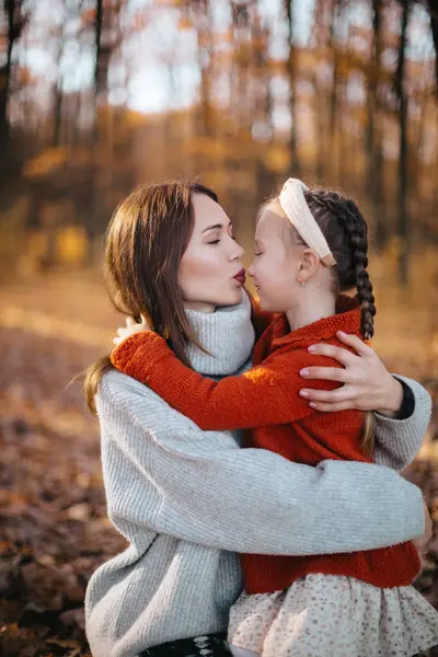 stock image Mother is hugging her daughter with braids in an autumn forest. The woman, dressed in a gray sweater and skirt, is hugging her little daughter, who is wearing a red sweater, in the autumn forest.