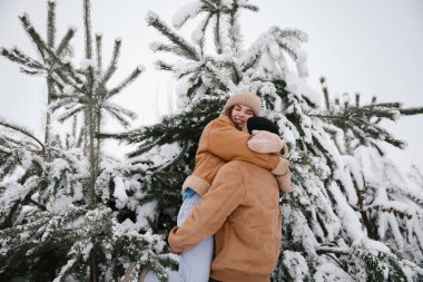 Sevgi dolu bir çift, karlı kış manzarasında sıcak bir kucaklaşmayı paylaşıyor. Etrafı çam ağaçlarıyla çevrili, doğada romantizm ve neşe dolu bir anı yakalıyor..