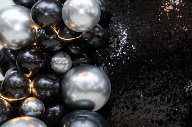Işıldayan pullar ve sıcak peri ışıklarıyla gösterişli siyah ve gümüş balon düzenleme. Zarif partiler, yeni yıl kutlamaları ve görkemli etkinlikler için mükemmel bir zemin..