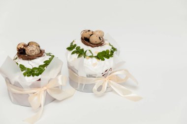 İki güzel dekore edilmiş Paskalya pastası, beyaz kremalı, bıldırcın ve altın yumurta içeren küçük yuvalarla süslenmiş, taze yeşil yapraklar, ve zarif saten kurdelelerle bağlanmış..