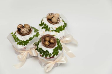 Elegant Easter cakes decorated with white icing, green leaves, and small nests filled with quail and golden eggs, tied with delicate satin ribbons. clipart