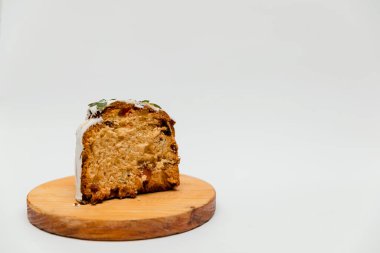 Dilimlenmiş beyaz kremalı, yeşil yapraklı bir Paskalya pastası, beyaz bir tabakta servis edilir, yumuşak dokusunu kurutulmuş meyvelerle, canlı sarı yumurtaların yanında festival sunumu için sunar..