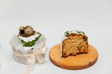 Beyaz kremalı, yeşil yapraklarla süslenmiş bir Paskalya pastası, iki canlı sarı yumurta ve ahşap bir tahtanın yanında, içinde kurumuş meyvelerin olduğu yumuşak, kabarık bir dokuyu ortaya çıkaran bir kesit..