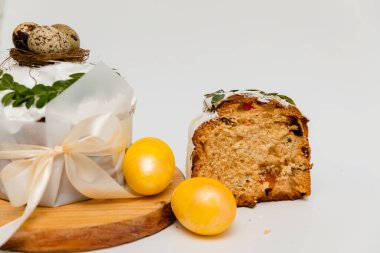 Beyaz kremalı, yeşil yapraklarla süslenmiş bir Paskalya pastası, iki canlı sarı yumurta ve ahşap bir tahtanın yanında, içinde kurumuş meyvelerin olduğu yumuşak, kabarık bir dokuyu ortaya çıkaran bir kesit..