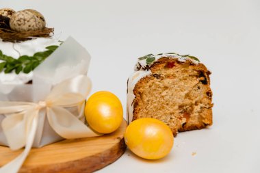 Beyaz kremalı, yeşil yapraklarla süslenmiş bir Paskalya pastası, iki canlı sarı yumurta ve ahşap bir tahtanın yanında, içinde kurumuş meyvelerin olduğu yumuşak, kabarık bir dokuyu ortaya çıkaran bir kesit..