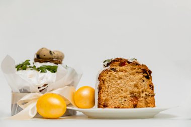 Beyaz kremalı, yeşil yapraklarla süslenmiş bir Paskalya pastası, iki canlı sarı yumurta ve ahşap bir tahtanın yanında, içinde kurumuş meyvelerin olduğu yumuşak, kabarık bir dokuyu ortaya çıkaran bir kesit..