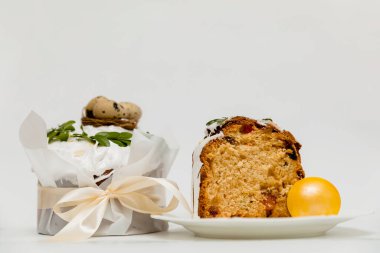 Beyaz kremalı, yeşil yapraklarla süslenmiş bir Paskalya pastası, iki canlı sarı yumurta ve ahşap bir tahtanın yanında, içinde kurumuş meyvelerin olduğu yumuşak, kabarık bir dokuyu ortaya çıkaran bir kesit..