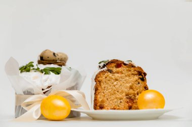 Beyaz kremalı, yeşil yapraklarla süslenmiş bir Paskalya pastası, iki canlı sarı yumurta ve ahşap bir tahtanın yanında, içinde kurumuş meyvelerin olduğu yumuşak, kabarık bir dokuyu ortaya çıkaran bir kesit..