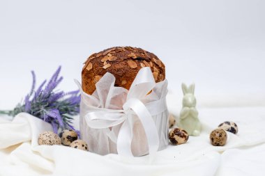 Geleneksel Paskalya ekmeği (kulich) üzerine beyaz parşömen kağıdına sarılı beyaz parşömen kurdelesi, yanında bıldırcın yumurtası ve mor lavanta filizi serpiştirilmiş açık kumaş arka plan..