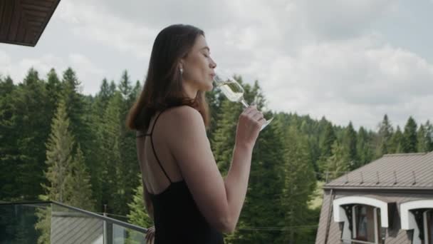 穿着晚礼服的女孩在Balcony旅馆喝香槟 美丽的自然景观和房子 奇形怪状的布莱内特与裸露的肩 — 图库视频影像