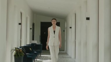 Beyaz Pantolon Giyen Model Otelin lobisinde yürüyor. Geniş pencereleri ve parlak sandalyeleri olan harika bir iç mekan. Uzun boylu esmer..