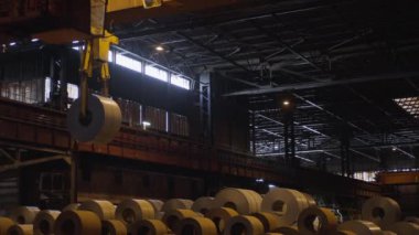 Geniş bir sanayi deposunda, etkileyici kağıt ruloları görülebilir, etkin bir vinç ile