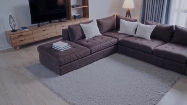 Burası modern bir oturma odası. Zarif mobilyalarla birlikte lüks, kahverengi bir kanepe sergiliyor.