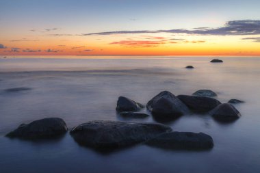 Kayalık bir sahil üzerinde kırmızı renkli gökyüzü. Gün batımı manzarası.