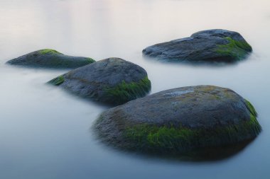 Gün batımından bir saat sonra. Pürüzsüz su ve düzensiz kayalar. Sakin deniz suyu. Uzun pozlama