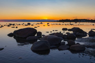 Deniz suyunda kayalıklar batıyor. Gün batımı, uzun pozlama. Baltık Denizi
