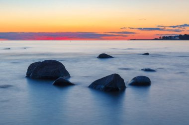 Deniz suyunda kayalıklar batıyor. Gün batımı, uzun pozlama. Baltık Denizi
