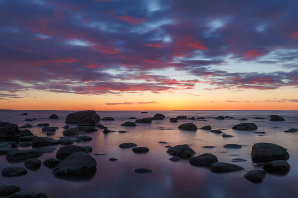 Late red sunset view of rocky sea shore, damatic light, long exposure