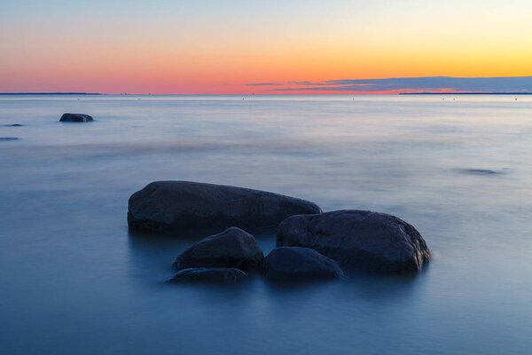 Rocky shore with stones sinking in the sea water. Sunset, long exposure. Baltic sea
