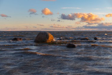 Gün batımında Baltık deniz taşları. Dalgalar sığ sularda.