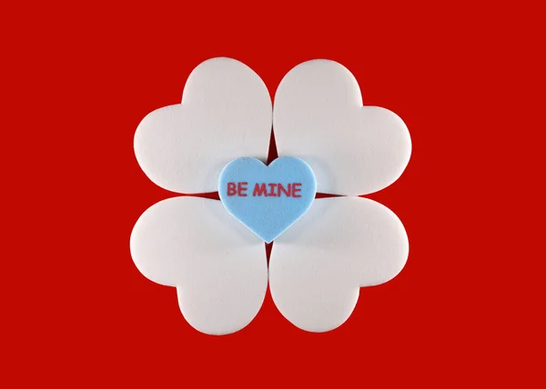 Be mine text on blue heart sitting on four white foam hearts on red background, Valentines day concept.