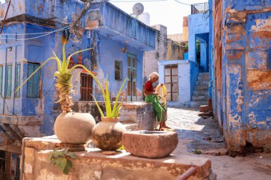 JODHPUR, INDIA - 17 Ekim 2022: Hindistan 'ın başkenti Rajasthan' daki Blue City Jodhpur 'da tarihi evler arasında boruları katlayan yaşlı kadın.