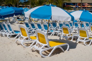 Yaz mavisi sarı plaj şemsiyeleri ve kumdaki sandalyeler, bir Karayip adası plajı..