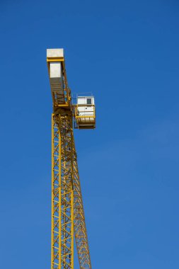 Mavi gökyüzüne karşı inşaat alanında uzun sarı bir vinç..