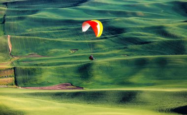 Colorful glider flying over rolling hills of Palouse ,Washington state, USA. clipart