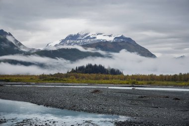 Scenic snow covered mountain landscape with low level clouds in Alaska during late autumn time. clipart