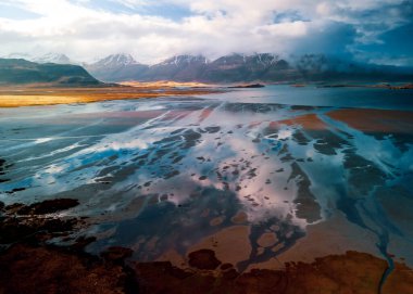 Baharda İzlanda kırsalındaki manzaralı nehir ve dağ manzarası.