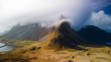 Panoramic view of low level cloud-covered mountains in Iceland's eastern shore line. clipart