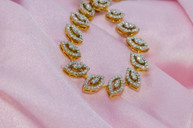 Pembe saten kumaş arka planda altın bir zincir üzerine dizayn edilmiş orijinal elmas yaprağın yakın plan çekimi.