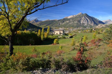 Briancon yakınlarındaki bir tepede bulunan Villard Saint Pancrace şapeli, Fransa 'nın Hautes Alpes (Fransız Güney Alpleri), sonbahar renkleriyle çevrili ve arka planda Briancon kasabası yer almaktadır.