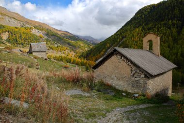 Le Villard köyü, Ceillac köyünün üzerindeki Cristillan vadisi boyunca yer alır, Queyras Bölgesel Doğal Parkı, Güney Alpleri, Fransa, Sainte Barbe şapeli, geleneksel ahşap bir dağ evi ve sonbahar renkleriyle