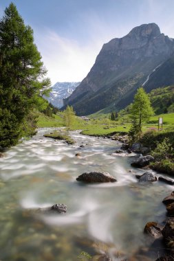 Dağ deresi Doron de Chaviere, Pralognan la Vanoise 'in yukarısındaki Chaviere vadisi boyunca yer alır, Vanoise Ulusal Parkı, Kuzey Fransız Alpleri, Tarentaise, Savoie, Fransa' nın arka planında Les Prioux köyü bulunur.