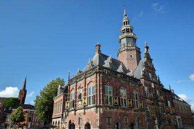 Arka planda Saint Franciscusbasiliek (Aziz Francis Bazilikası) çan kulesi ile, Hollanda, Bolsward Rönesans tarzı belediye binasının süslü ve renkli mimarisi