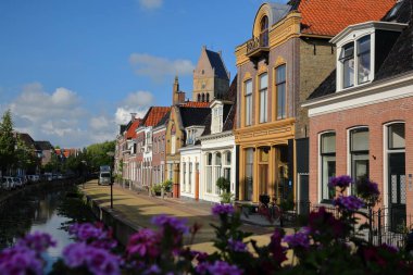 Bolsward, Friesland, Hollanda 'da Kleine Dijlakker caddesi boyunca renkli ev cepheleri, arka planda Martinikerk çan kulesi (St Martin kilisesi) bulunuyor.