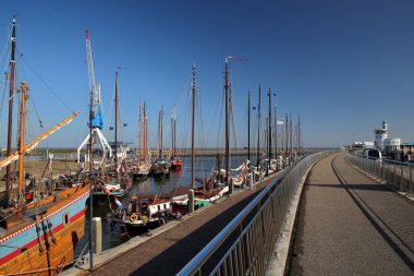 Harlingen, Friesland, Hollanda 'daki ana limana ve tren istasyonuna giden yürüyüş yolu, solda demirleyen eski ahşap yelkenli tekneler ve liman vinçleri var.
