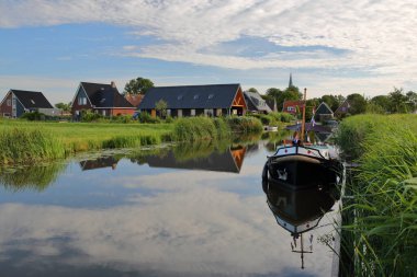 Leeuwarden 'ın 13 km batısındaki Baard, Friesland, Hollanda' daki bir kanalda bulunan evlerin yansıması ve bir demirleme teknesi.