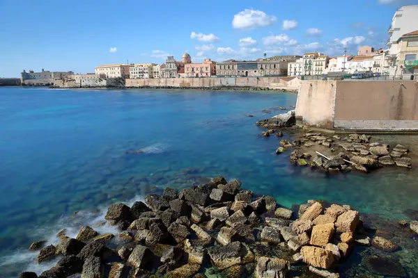 Ortigia Adası 'nın doğu kayalık kıyıları, Syracuse, Sicilya, İtalya, berrak ve renkli su ve solda Castello Maniace (Maniace kalesi) ile