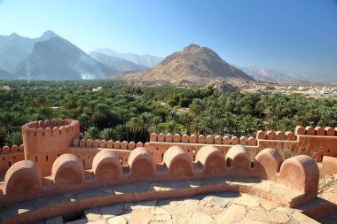 Etkileyici Nakhal kalesi, Al Batinah, Umman, kuleleri ve surlarıyla, palmiye koruluğuna bakan ve dağlarla çevrili